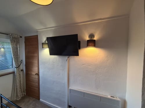 Modern studio apartment bedroom at 2 Doves, Exeter with wall-mounted TV, ambient lighting, and textured white walls
