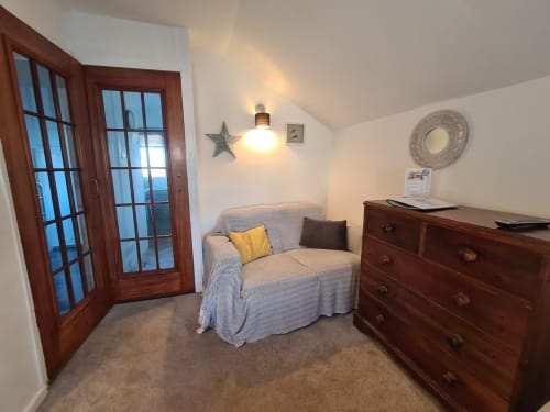 Cozy Garret Studio Apartment in Topsham with comfortable bed, wooden dresser, and glass doors opening to balcony views.