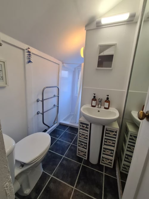 Modern bathroom at 2 Doves Holiday Property Exeter with toilet, pedestal sink, shower, and dark tiled floor