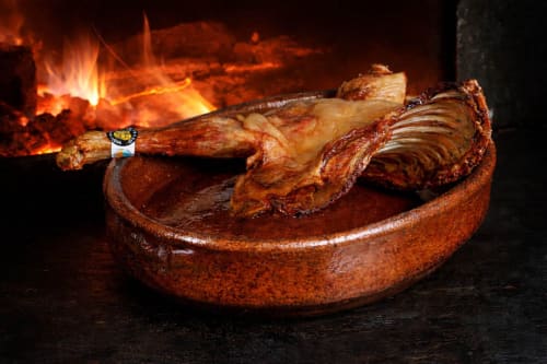 Lechazo asado servido en cazuela de barro junto al fuego