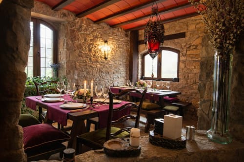 Comedor de piedra con mesas preparadas y lámpara colgante junto a ventanas arqueadas