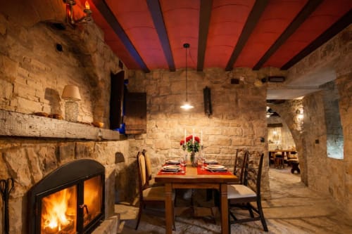 Mesa preparada junto a una chimenea en un comedor de piedra con vigas de madera