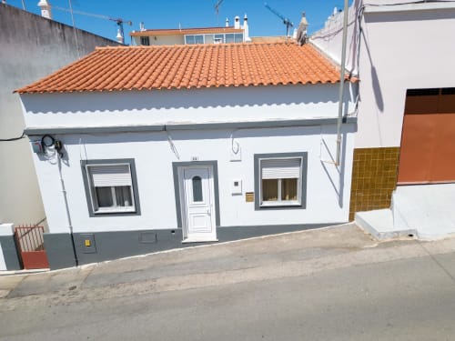 Villa branca com telhado de terracota em Urban Beach Rentals, Portugal. Vista da rua da acomodação com vista para o jardim.