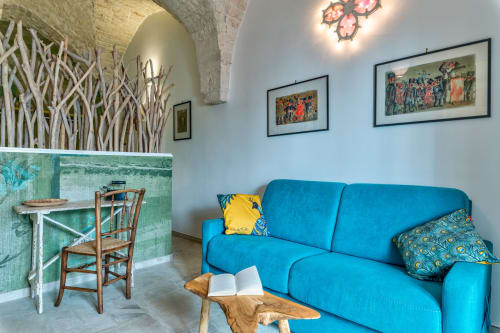 Divano azzurro luminoso nella camera ospiti Pietra & Luce a Ostuni, con arredi in legno e opere d'arte incorniciate