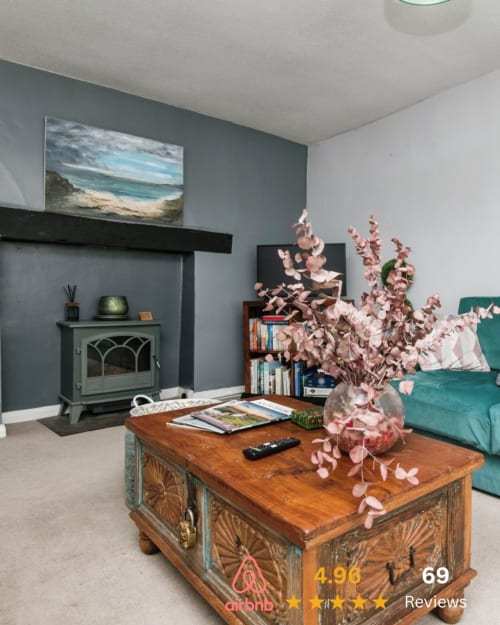 Cozy Exeter holiday rental lounge with teal stove, wooden coffee table, pink dried flowers, and coastal beach artwork