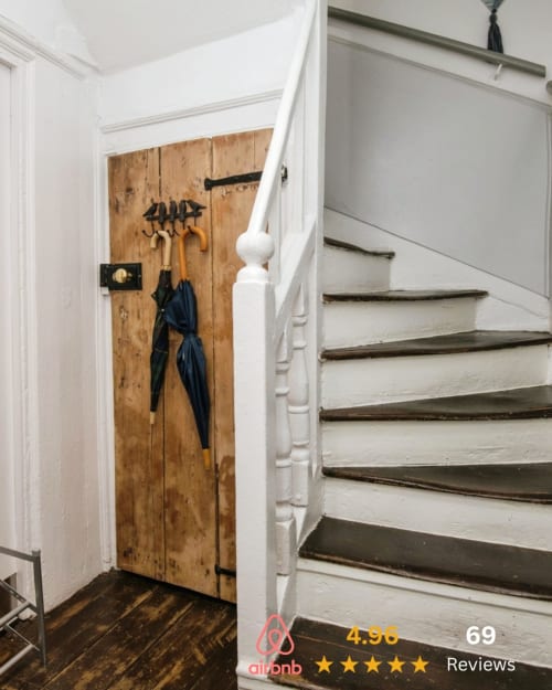 Staircase landing with wooden storage closet, umbrellas, and tool hooks at 2 Doves Holiday Property, Exeter