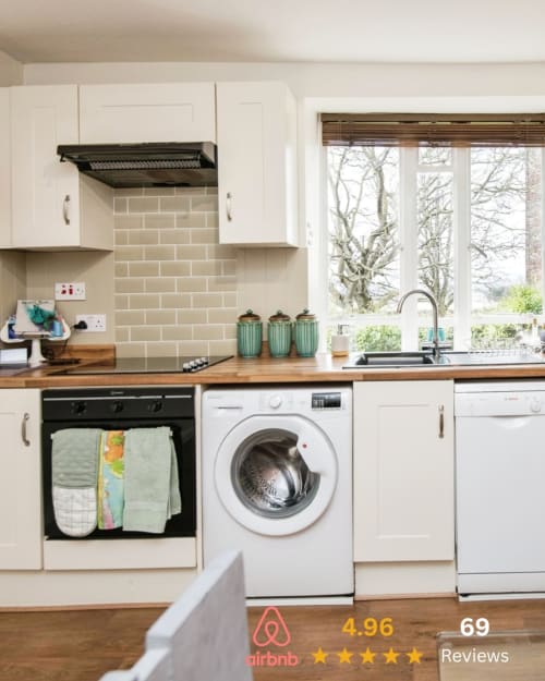 Modern Exeter kitchen at 2 Doves Holiday Property with white cabinets, wood counters, black range hood, washing machine, and