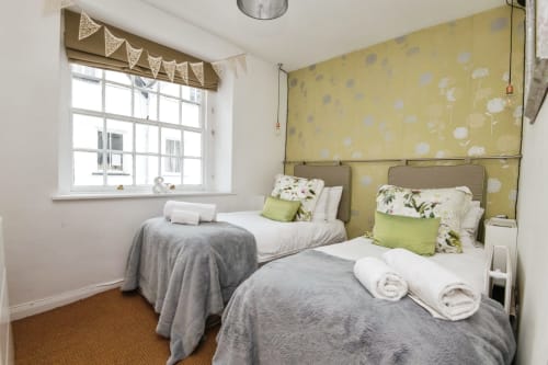 Twin bedroom at 2 Doves Holiday Property, Exeter with grey bedding, yellow floral wallpaper and window view.