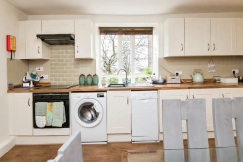 Modern kitchen at 2 Doves Holiday Property, Exeter with white cabinets, wood counters, and view of bare trees through large