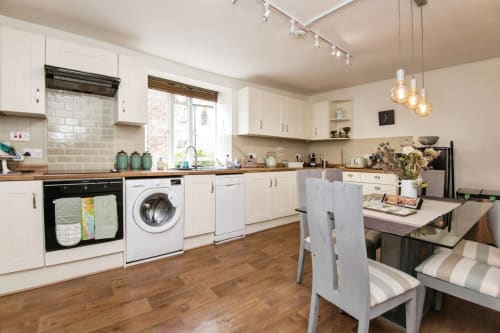 Modern kitchen with white cabinets, wooden counters, dining area and appliances at 2 Doves Holiday Property in Exeter