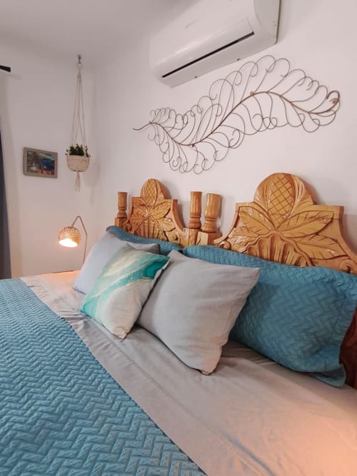 Dormitorio tropical con cabecero de madera tallada, ropa de cama acolchada azul y arte decorativo de hojas de alambre en Casa Punta Perula,
