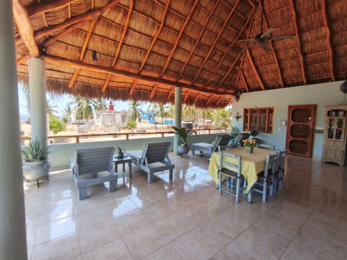 Terraza con vista al océano de Casa Punta Perula con techo de palapa, mesa de comedor, tumbonas y vistas costeras en Punta Perula,