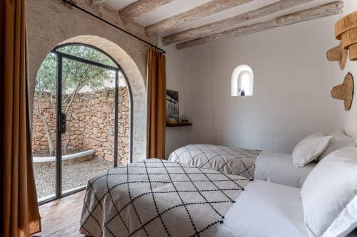 Bright bedroom at Domaine Belhazar cottage in Essaouira with twin beds, arched doorway, exposed wooden beams, and stone