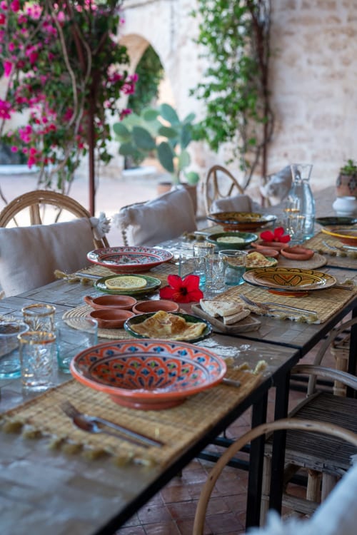 Outdoor dining table at Domaine Belhazar, Essaouira with colorful Moroccan plates, flowers, and stone architecture