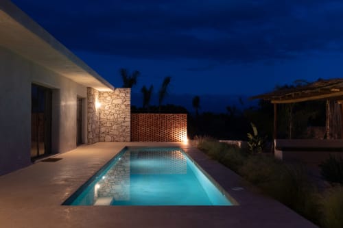 Illuminated pool at Domaine Belhazar, Essaouira. Modern apartment pavilion with stone walls and terrace at twilight.