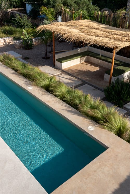 Turquoise swimming pool with ornamental grasses and thatched-roof cabana at Domaine Belhazar, Essaouira