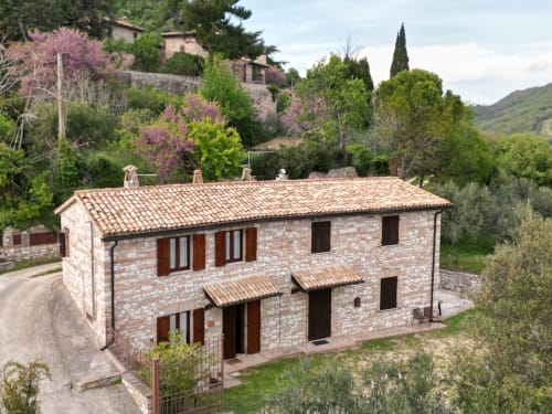 Villa in pietra toscana Le Colline della Speranza in Umbria, con tetto in cotto, circondata da giardini fioriti e colline