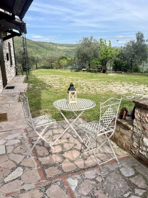 Terrazza esterna con arredamento in metallo bianco e pavimentazione in pietra che si affaccia su lussureggianti giardini e colline umbre a Le Colline della