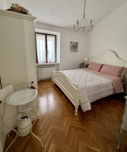 Camera da letto elegante con letto color crema, biancheria rosa, parquet a spina di pesce, lampadario e bagno ensuite a Le Colline della