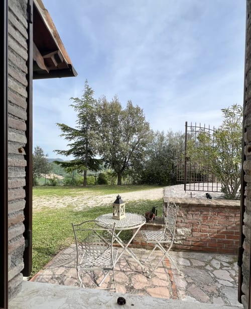 Terrazza nella campagna toscana con sedute in ferro battuto, lanterna e viste sul giardino a Le Colline della Speranza, Spello