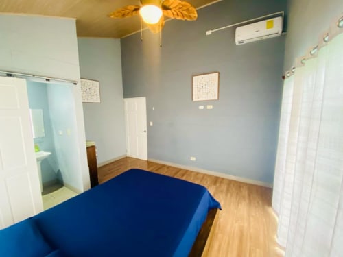 Dormitorio luminoso con cama azul, pisos de madera y paredes azul claro en la villa Cabinas Arenal Home, Costa Rica
