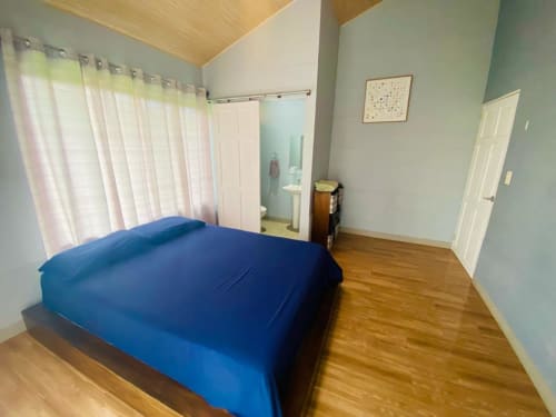 Espacioso dormitorio en villa Cabinas Arenal Home con cama azul, pisos de madera, baño privado y vistas al jardín
