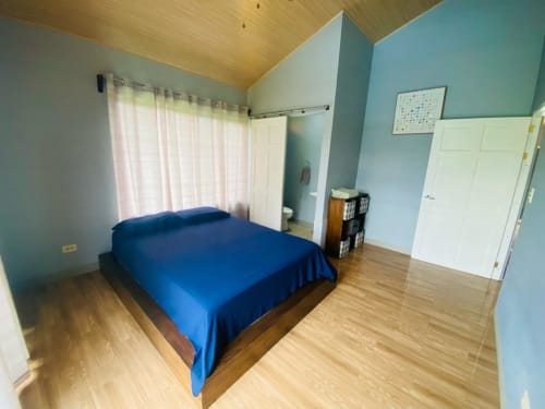 Espaciosa habitación en villa Cabinas Arenal Home con cama azul, pisos de madera, paredes turquesas y vistas al jardín