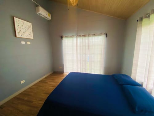 Habitación espaciosa en villa Cabinas Arenal Home con cama azul, piso de madera, aire acondicionado y vistas al jardín