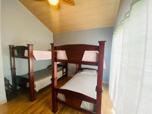 Luminosa habitación con dos camas litera de madera, ropa de cama blanca, techo de madera con ventilador y persianas en Cabinas Arenal Home