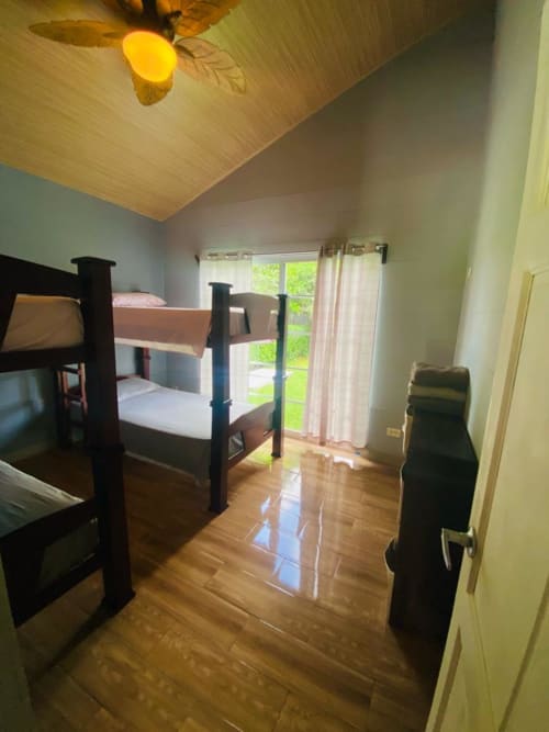 Dormitorio de la villa Casa de las Rosas con cama litera, ventilador de techo de madera y puertas con vista al jardín en Cabinas Arenal Home, Costa Rica