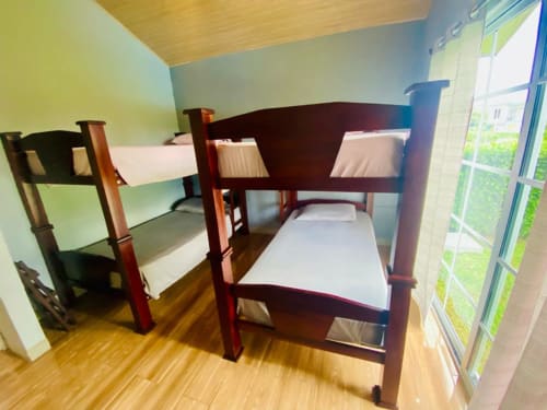Acogedora habitación de villa en Cabinas Arenal Home con literas de madera, ropa de cama blanca, paredes verde pálido y vista al jardín en Costa
