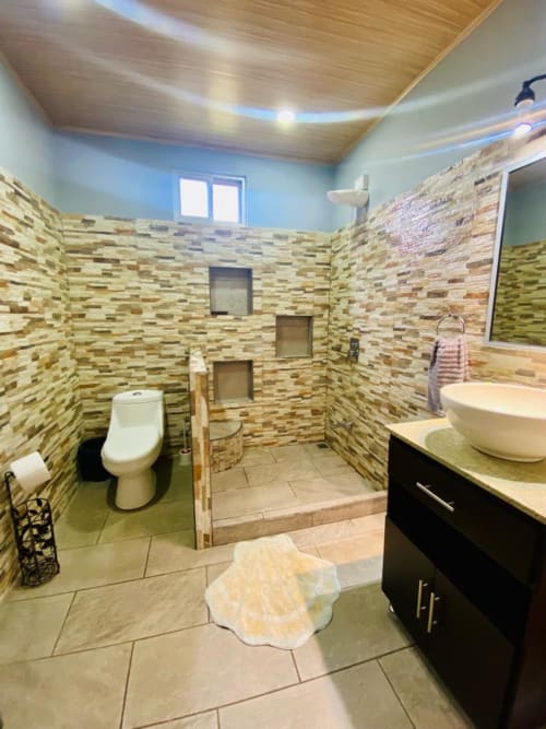 Baño moderno en villa Cabinas Arenal Home con muros de piedra, ducha tipo caminador, inodoro y lavamanos tipo vasija