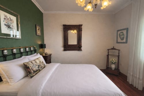 Elegante dormitorio en  Baiona con cama blanca, cabecero verde, espejo ornamentado y muebles clásicos
