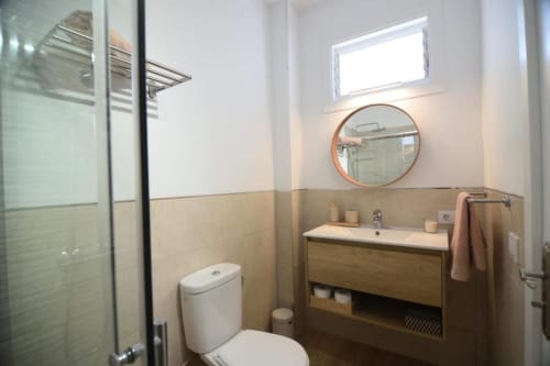Modernes Badezimmer in der Wohnung Bahía Anaga 703, Santa Cruz de Tenerife, mit Holzwaschtisch, rundem Spiegel und Glasdusche