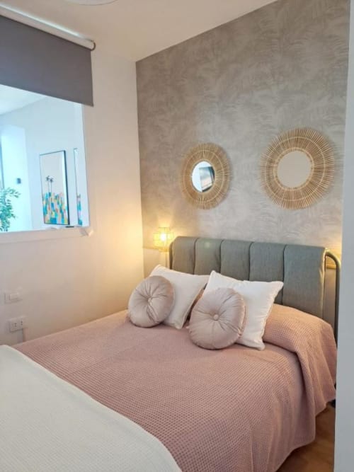 Modernes Schlafzimmer mit grauem Polsterbett, rosa Bettwäsche, dekorativen Spiegeln und warmer Beleuchtung in Santa Cruz de Tenerife
