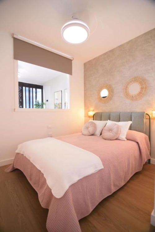 Modernes Schlafzimmer im Bahía Anaga 703 mit rosafarbenem Bettzeug, grauem Kopfteil, runden Spiegeln und runder Deckenleuchte