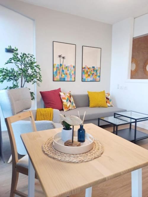 Modernes Wohnzimmer mit grauem Sofa, Holzesstisch, bunten Kissen und Palmenkunstwerk auf Teneriffa