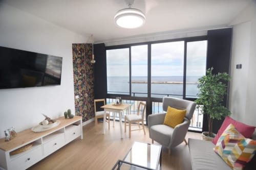 Modernes Wohnzimmer mit Meerblick-Balkon, ausgestattet mit grauem Sessel, Esstisch und TV in Santa Cruz de