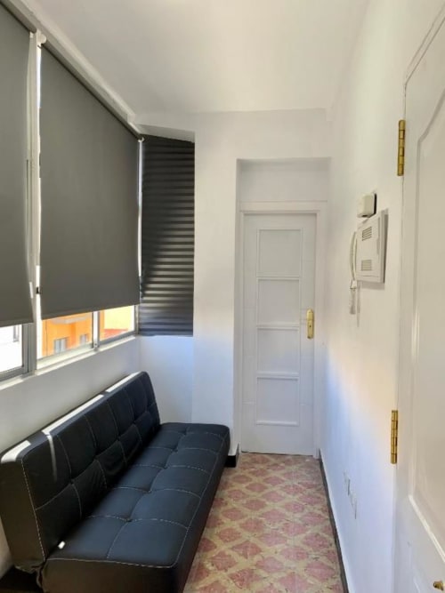 Moderner Wohnungsflur mit schwarzem Sofa, Fenster mit Stadtblick, weißen Türen und Fliesenbelag in Santa Cruz de Tenerife