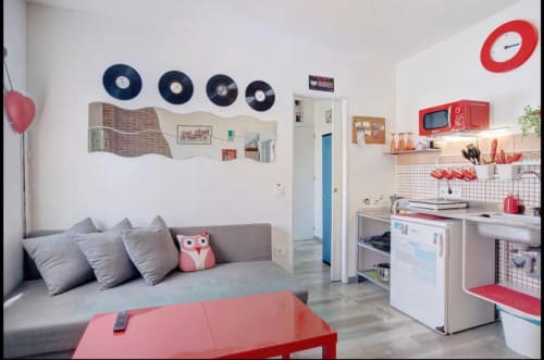 Stilvolles Studio-Apartment in Santa Cruz de Tenerife mit grauem Sofa, roten Akzenten, Kochnische und Vinyl-Schallplatten-Wanddekoration.