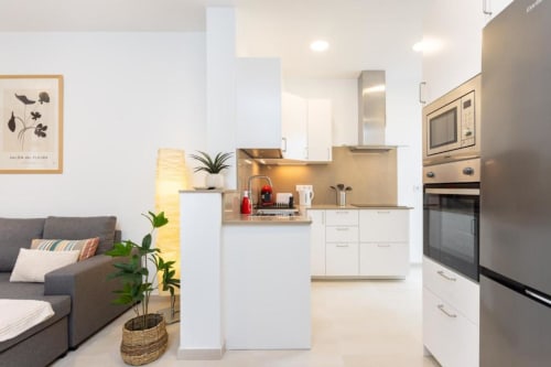 Modernes offenes Apartment mit Wohnküche, weißen Schränken, Edelstahlgeräten und grauem Sofa in Santa