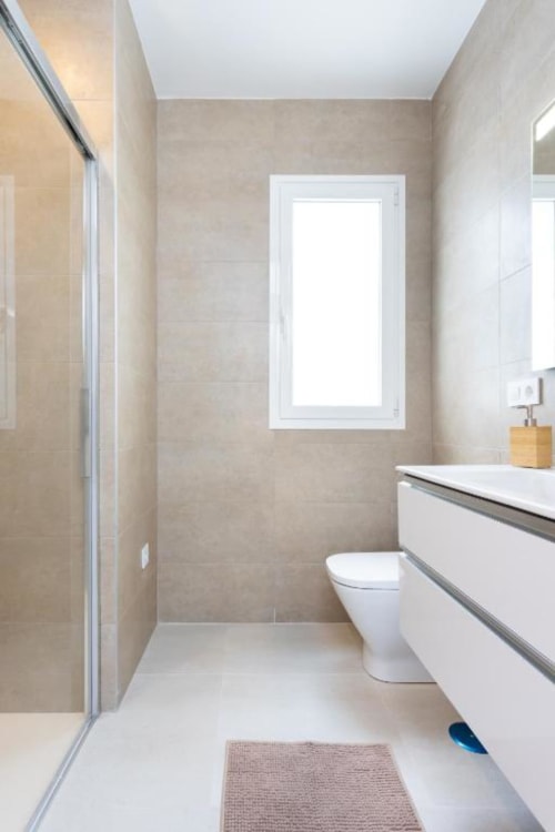 Modernes Badezimmer mit weißem Waschtisch, Toilette, beigen Fliesenwänden, Duschkabine und Fenster im Apartment Triana Toscal, Santa