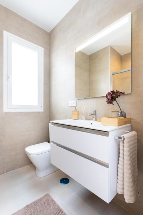 Modernes Badezimmer in Santa Cruz de Tenerife mit weißem Waschtisch, Spiegel, Toilette und beigen Fliesenwänden