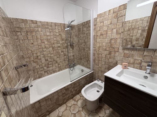 Modern bathroom at Chez Francine in Notre Dame de Bellecombe with tiled walls, bathtub with shower screen, sink, and bidet.