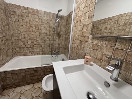 Modern bathroom with white sink, toilet, and bathtub with brown tile walls at Chez Francine apartment in Notre Dame de