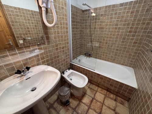 Bathroom at Chez Francine studio apartment with sink, bidet, bathtub shower and brown tile walls in Notre Dame de Bellecombe