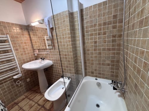 Modern bathroom with brown tile walls, pedestal sink, bidet, and walk-in shower at Chez Francine apartment, Notre Dame de