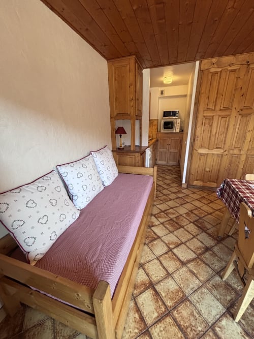 Cozy studio apartment bedroom at Chez Francine with wooden bed, pink bedding, wooden ceiling, and kitchenette visible through