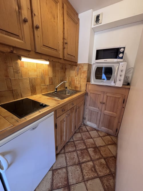 Compact kitchen in Chez Francine studio apartment with wooden cabinets, tiled backsplash, and essential appliances including