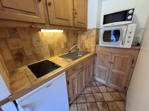Studio kitchen at Chez Francine with wooden cabinets, tiled backsplash, microwave, and compact appliances in Notre Dame de